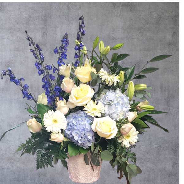 Bouquet of cream roses, blue hydrangeas, and white daisies in a pink vase