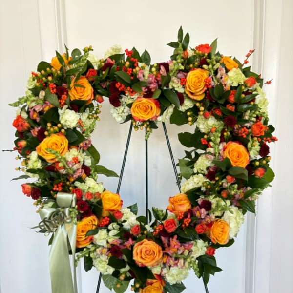 Heart-shaped floral wreath with orange roses and mixed blooms on a stand