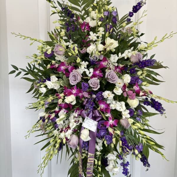 Large standing spray of purple, white, and pink flowers on a white easel