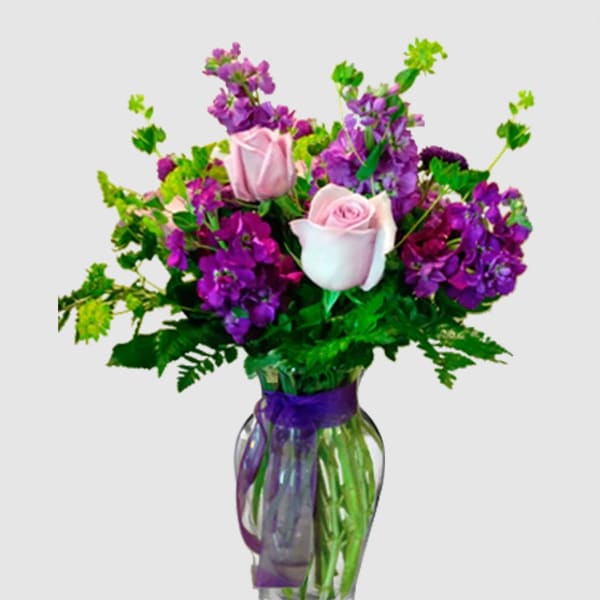 Pink roses and purple flowers arranged in a glass vase with a purple ribbon
