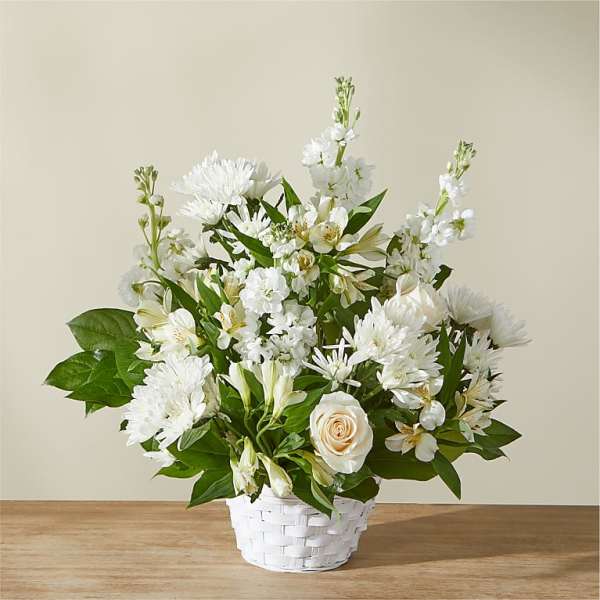 White floral arrangement in a white basket with green leaves