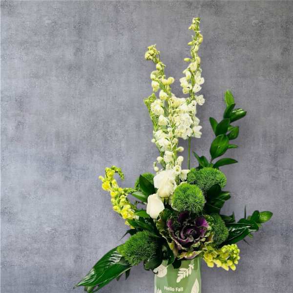 Tall floral arrangement with white blooms and green accents in a green container