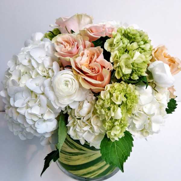 Bouquet of white hydrangeas, peach roses, and green blooms in a glass vase