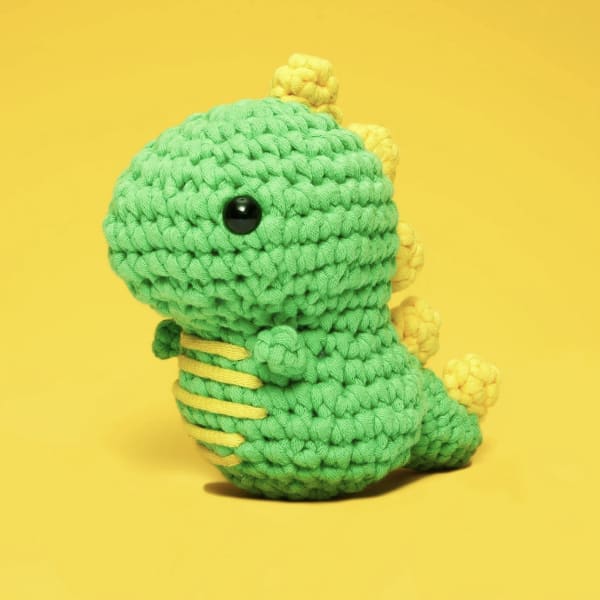 Crocheted green dinosaur plush with yellow accents on a yellow background