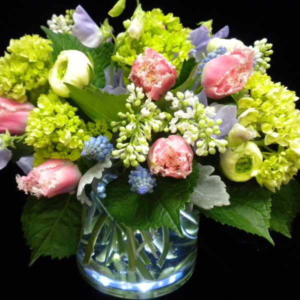 Low glass vase of pink fringe tulips, green hydrangeas, lilac, and pastel blooms in a rounded arrangement