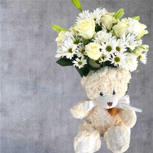 Teddy bear holding a bouquet of white flowers and pale yellow roses