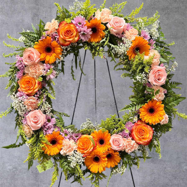 Circular floral wreath with pink roses and orange gerbera daisies on a stand