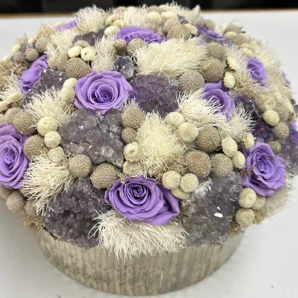Purple roses arranged with dried beige accents in a round box