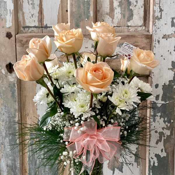Peach roses and white daisies in a tall green glass vase with a pink bow