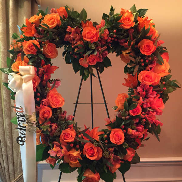 Orange rose wreath on a black stand with a white ribbon
