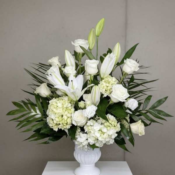 Large white arrangement of roses, lilies, hydrangeas, and carnations in a white pedestal vase