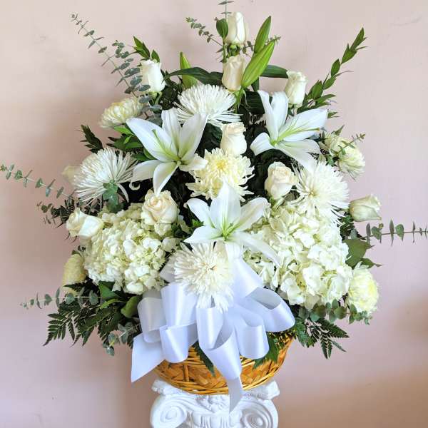 White floral arrangement in a woven basket with a large white ribbon