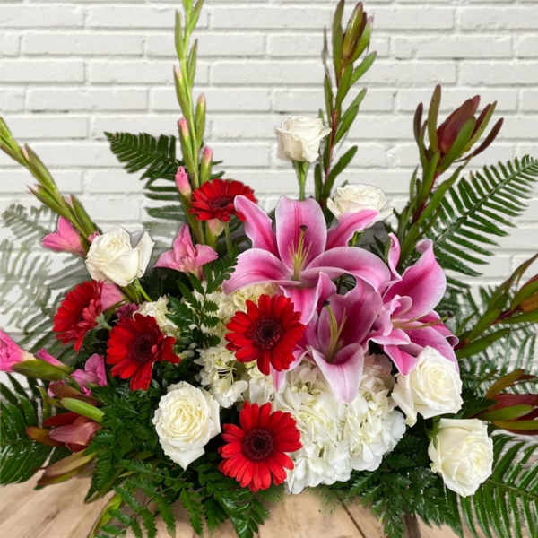 Pink lilies, red gerbera daisies, and white roses in a low arrangement