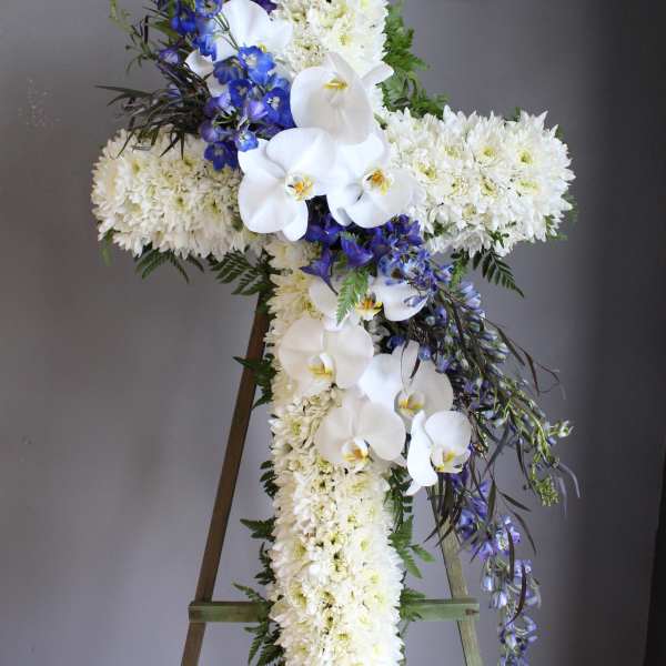 White floral cross arrangement with blue flowers on an easel