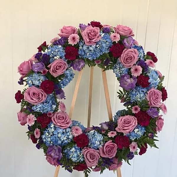 Circular floral wreath on a wooden easel with pink, blue, purple, and red blooms