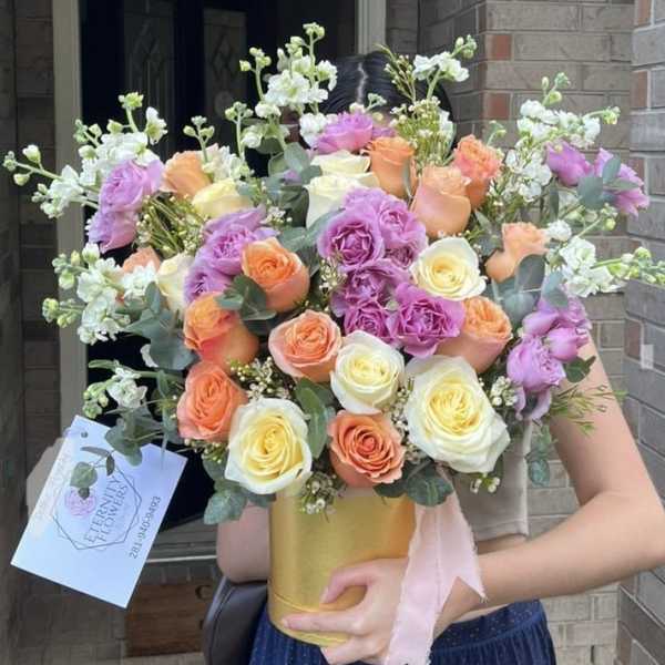 Bouquet of peach, lavender, and white roses in a gold vase