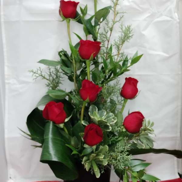 Tall arrangement of red roses in a black vase with greenery