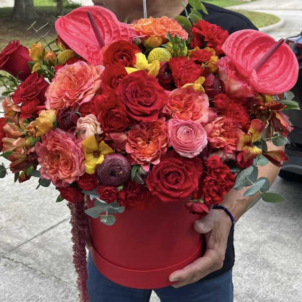 Large red and pink flower arrangement in a red hatbox with anthuriums and roses