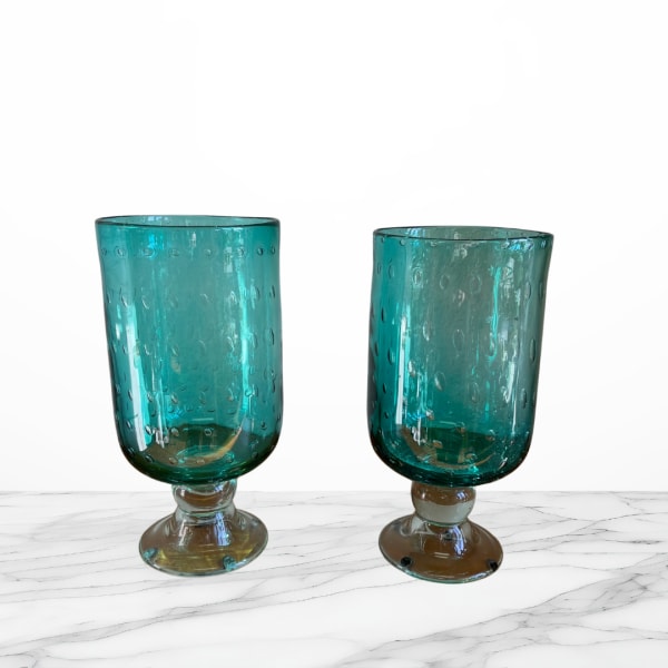 Two teal glass goblets with short stems on a white surface