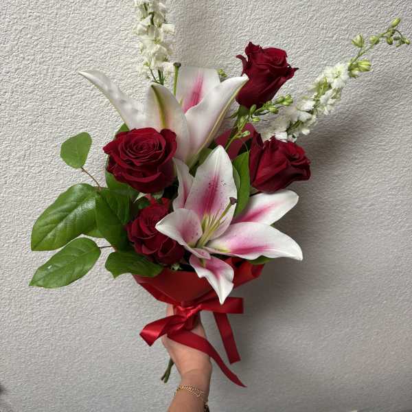 Hand-tied bouquet of red roses and pink lilies with a red ribbon