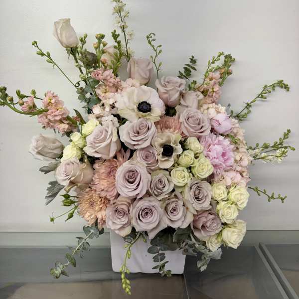 Large pastel floral arrangement in a white vase with roses and anemones