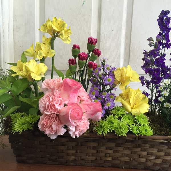 Mixed flowers in a rectangular wicker basket with pink, yellow, purple, and white blooms