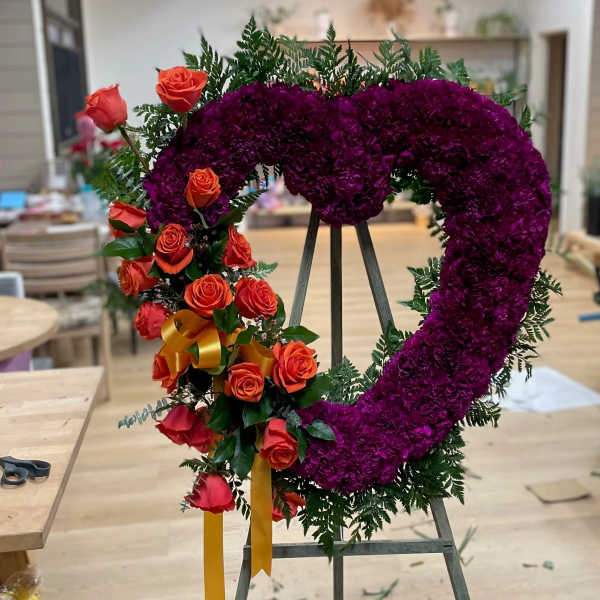 Heart-shaped floral wreath with purple blooms and orange roses on an easel