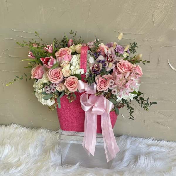 Pink and white flower arrangement in a bright pink handbag-style container with ribbon