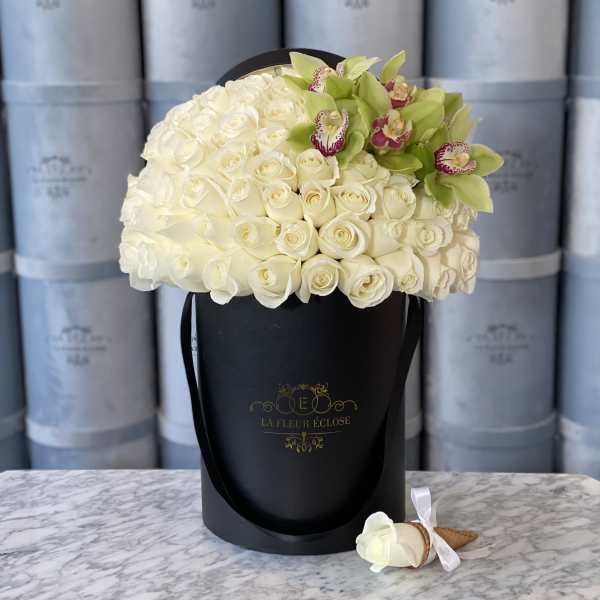 White rose arrangement in a black hat box with green orchids