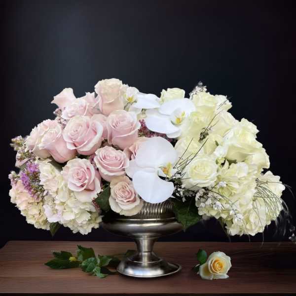 Pink and white roses with orchids in a silver pedestal vase