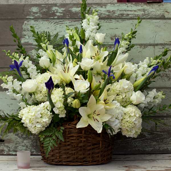 White lilies and roses in a wicker basket with blue iris accents