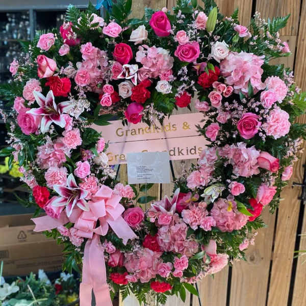 Heart-shaped floral wreath with pink roses, carnations, and lilies on an easel