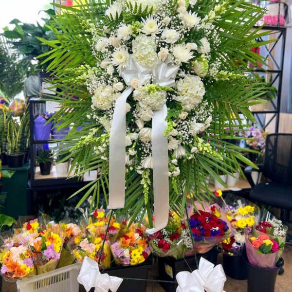 Large white floral standing spray with palm fronds and a white ribbon