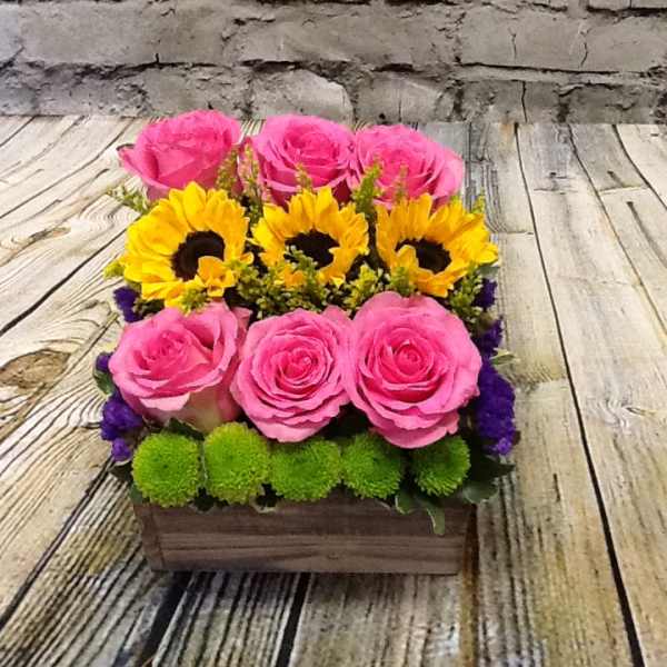 Pink roses and yellow sunflowers arranged in a wooden box
