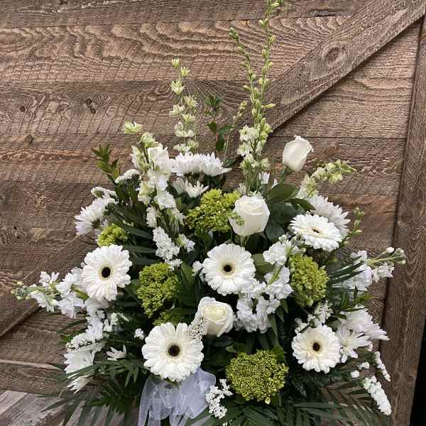 White and green floral arrangement in a white vase with a ribbon