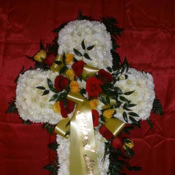 Cross-shaped floral tribute with white flowers, red roses, and gold ribbon
