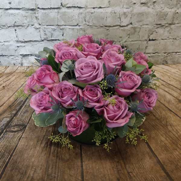 Pink rose bouquet with blue thistle accents on a low base