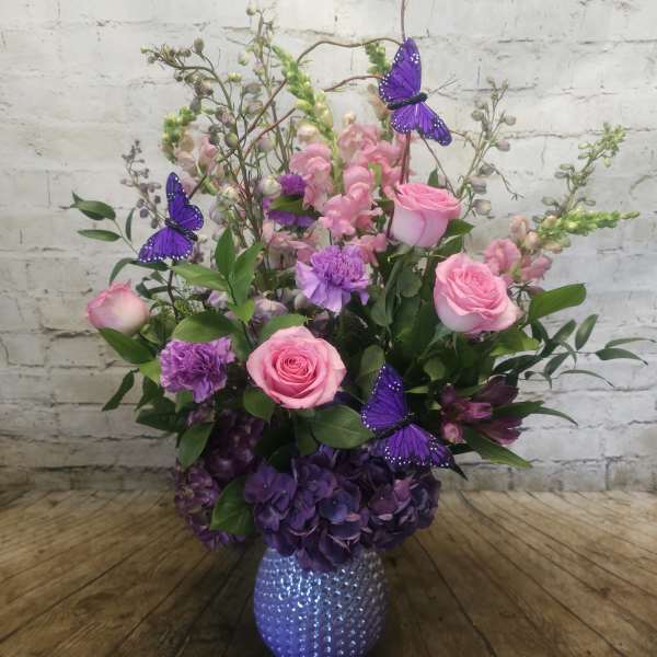 Pink roses and purple flowers in a textured vase with butterfly picks