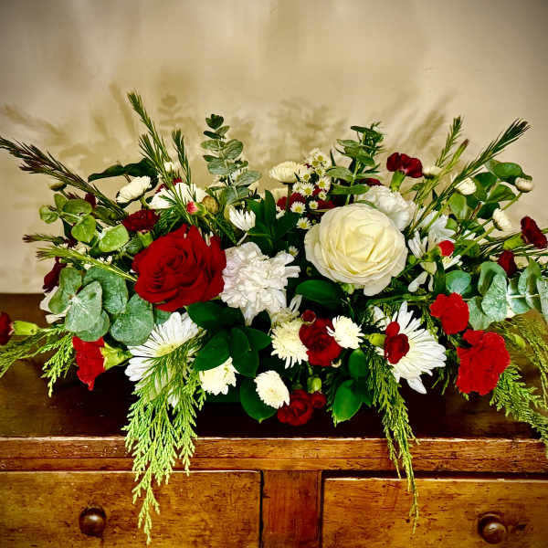 Low red and white flower arrangement with abundant greenery on a wooden dresser