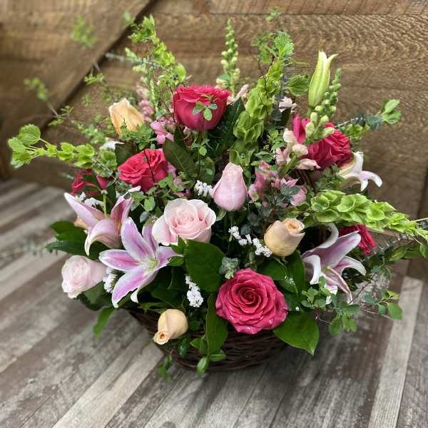 Basket arrangement of pink roses and lilies with greenery