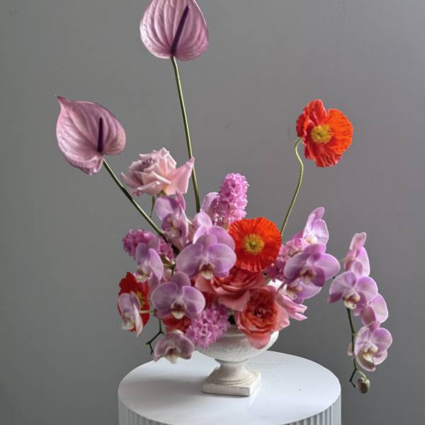 Pink and red floral arrangement in a white pedestal vase