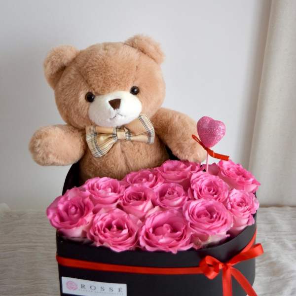 Pink roses in a black box with a teddy bear and heart topper