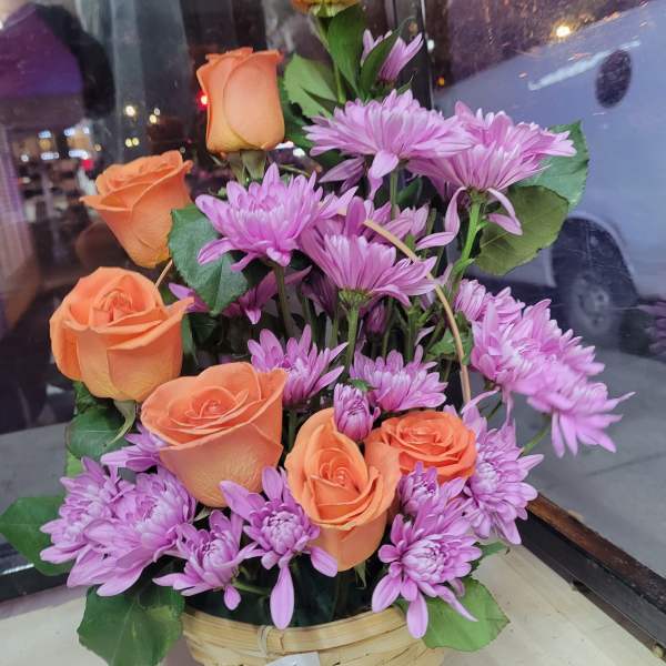 Basket arrangement of orange roses and purple daisies