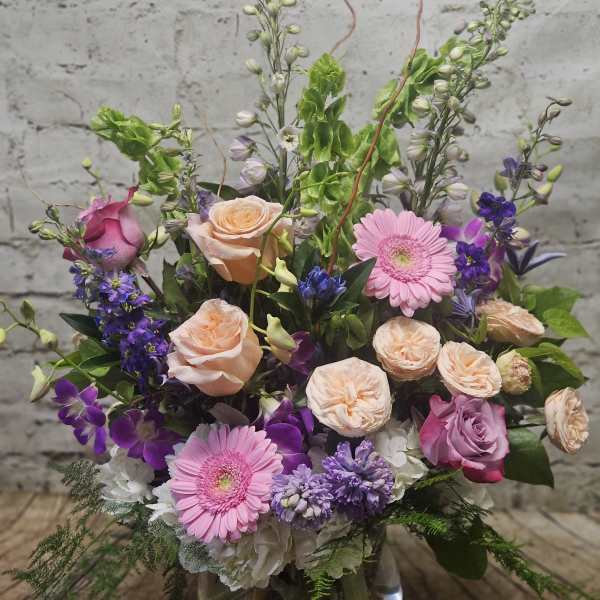 Mixed pink, purple, and peach flowers arranged in a glass vase