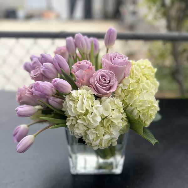 Lavender tulips and roses with pale hydrangeas in a clear glass vase