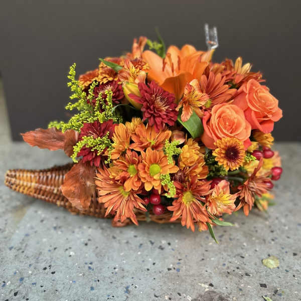 Orange and burgundy floral arrangement in a wicker basket