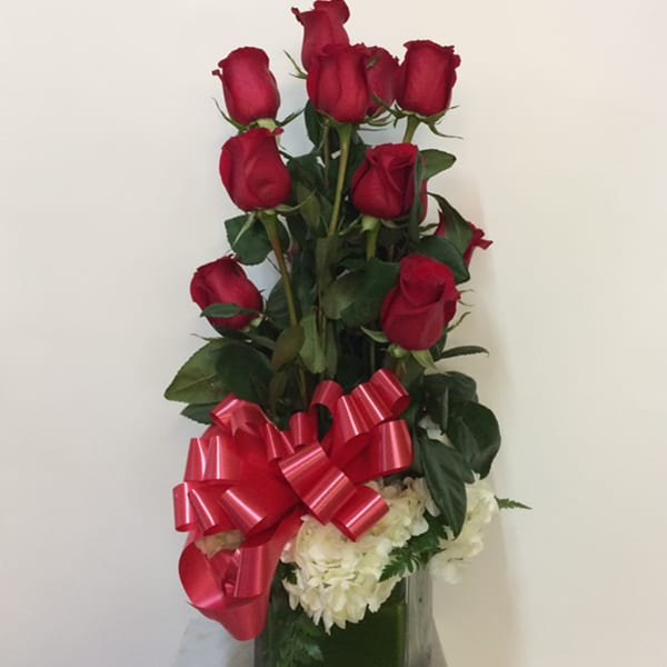 Tall arrangement of red roses with white flowers in a glass vase and red bow