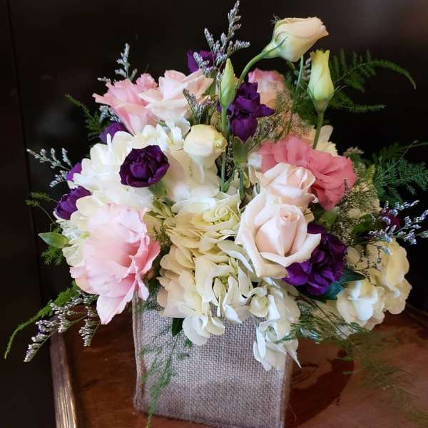 Pink, white, and purple floral arrangement in a burlap-wrapped container