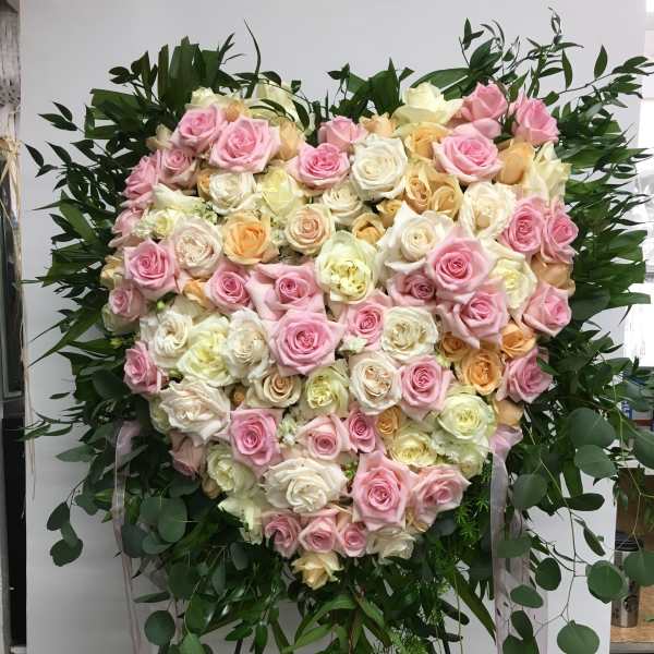 Heart-shaped arrangement of pink, white, and peach roses on a stand