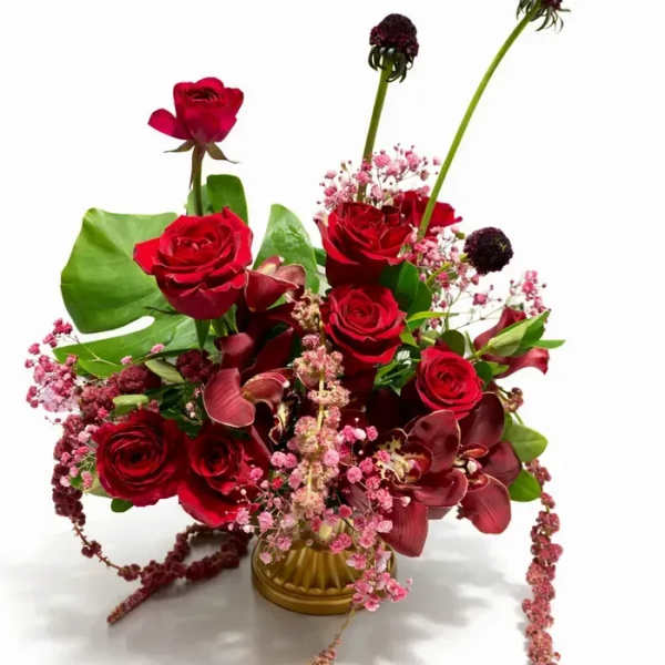 Red roses and pink filler flowers arranged in a gold vase